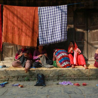 A group of women engaged in textile weaving on a vibrant street, showcasing traditional skills.