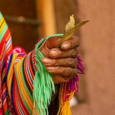 Close-up of a hand holding ritual leaves in colorful Andean textile, Cusco.